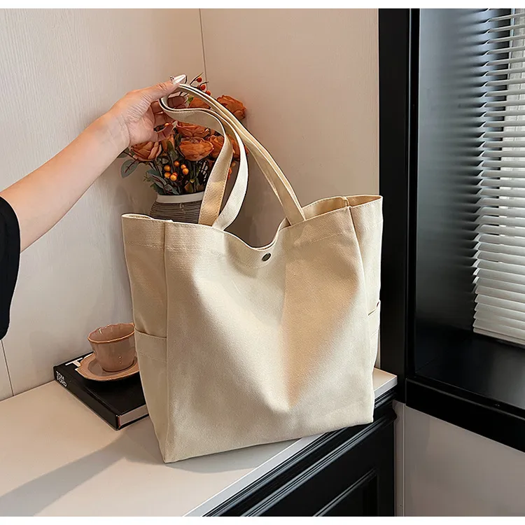 Cream canvas tote supported by a hand and windowsill; whole bag and both handles visible