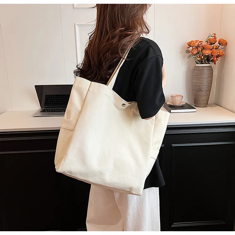 Cream canvas tote worn over one shoulder, photographed from behind without a face