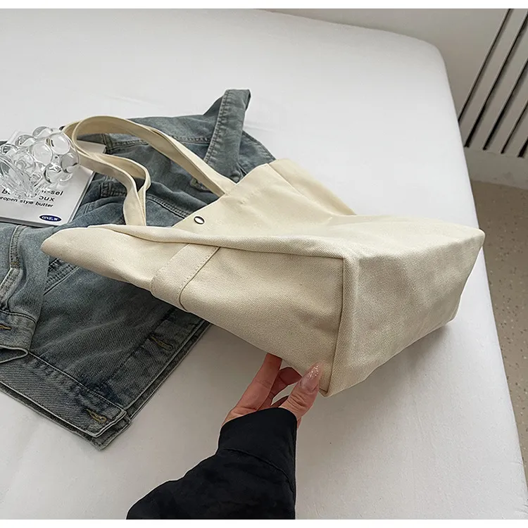 Cream tote turned to show the box-shaped base and side seams, supported on a surface
